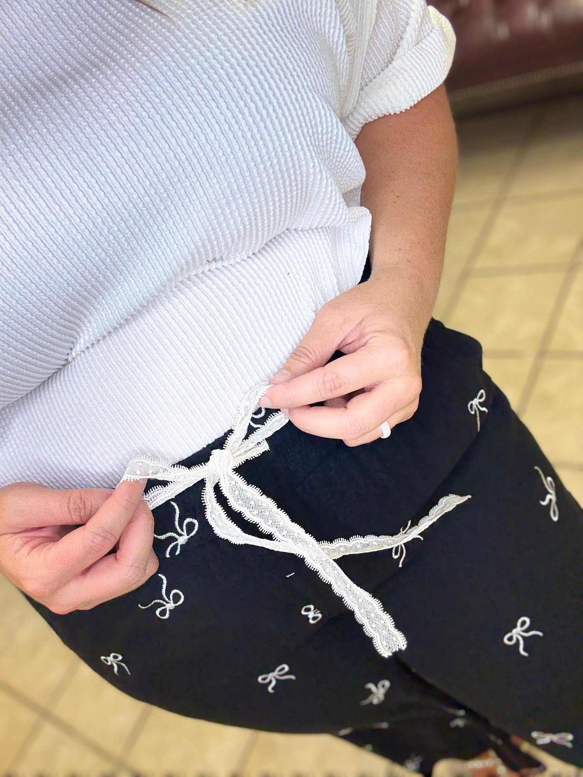 Woman wearing black wide leg linen blend pants with bow print and drawstring waist styled casually indoors