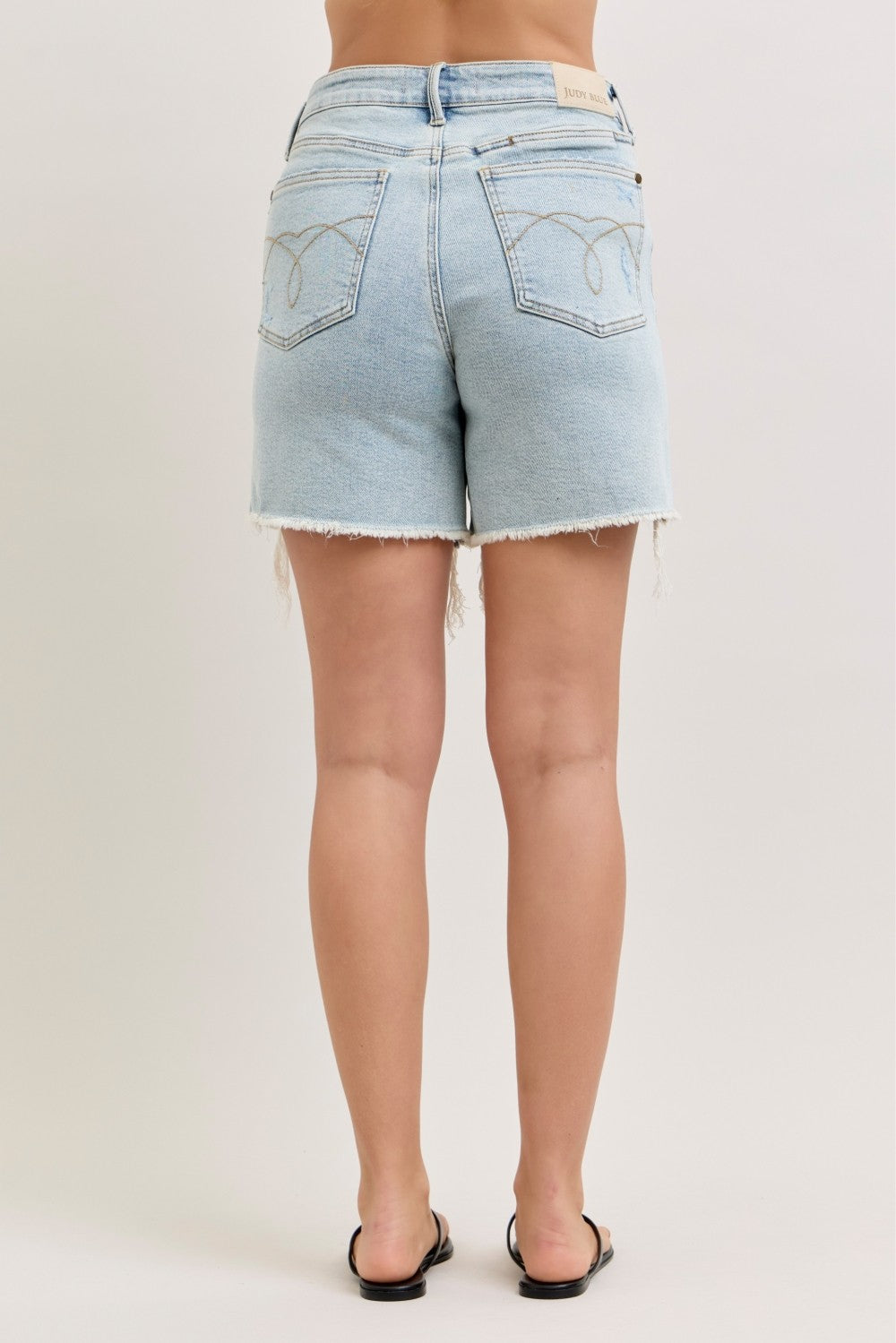 High waisted light wash distressed denim dad shorts with raw hem and relaxed fit front and back view on model outdoors